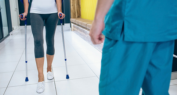 person using crutches walking in a hallway with healthcare professional in view rehabilitation therapy support 2
